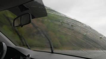 vista desde el interior de un coche que conduce a lo largo de la carretera en el parabrisas con limpiaparabrisas en funcionamiento durante la lluvia. el concepto de vehículos y conductores. nadie. video