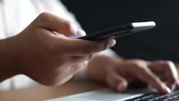 hand typing on laptop on office desk while holding smartphone video