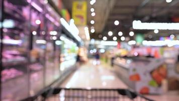 unscharfer und Trolley-Einkaufswagen, der sich durch Lebensmittelregale im Innenraum bewegt, defokussierter Hintergrund im Supermarkt. Person, die einen Einkaufswagen in einem Supermarkt in Zeitlupe schiebt. video