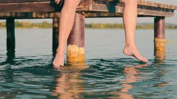 Uomini piedi nel il lago. un' uomo seduta su un' ponte con il suo gambe penzoloni nel il acqua. video