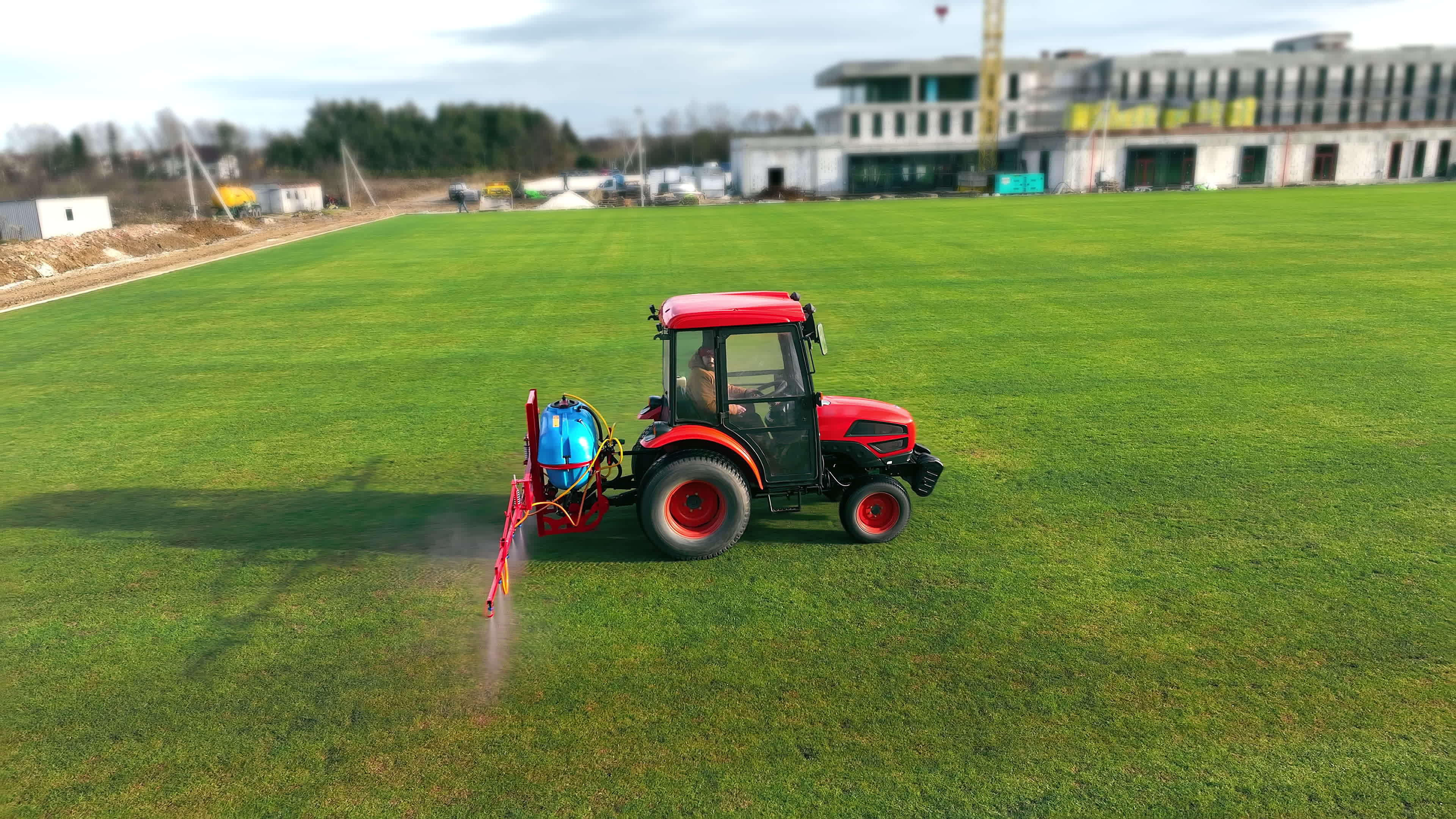 The tractor sprinkles the grass of the football field. Maintenance of
