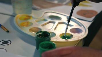 en barn. de konstnär späds ut grön måla med vatten, närbild video