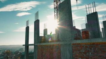 Construction engineers work on the construction of a house made of monolith and brick floors. Contrast sun rays shine into the camera. video
