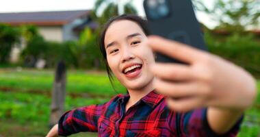 toma de mano, una agricultora usa una camisa a cuadros hablando en un teléfono inteligente para ver la transmisión de video, revisa su granja de vegetales orgánicos, sonríe con un agricultor feliz e inteligente con el concepto de dispositivo tecnológico video