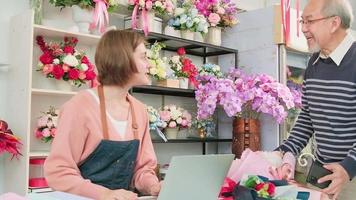 Cashless business entrepreneur. Asian elderly male customer shop and digital payments by scanning a mobile phone application to a White female florist owner. Beautiful floral shop, smart SME store. video