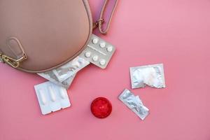 Birth control pill, vaginal candles, and condom peeking out from pocket handbags on a pink background. Flat lay. Top view. photo