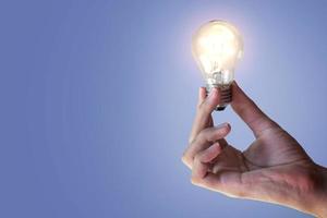 hand holding an incandescent light bulb isolated on blue background. Generate great ideas. illuminated light bulb. photo