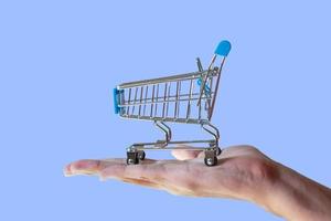 shopping cart in people's hand isolated on blue background. sales strategy concept. shopping promotion concept.