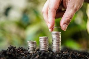 woman's hand is putting silver coins on pile silver coins with green nature background. money saving and business finance concept, business growth and money future, financial success photo