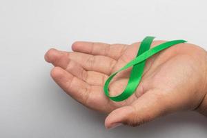 Green ribbon in hand.treatment concept for ovarian cancer and cervical cancer. photo