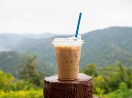 A glass of iced coffee is placed on the fence against a backdrop of mountains and sky. photo