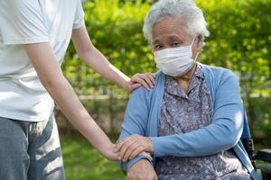 Caregiver help and care Asian senior or elderly old lady woman patient sitting on wheelchair in park, healthy strong medical concept. photo