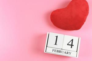 endecha plana de calendario de madera el 14 de febrero con almohada en forma de corazón rojo sobre fondo rosa, concepto de día de san valentín. foto