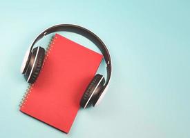 flat lay of red notebook covered with headphones on blue background  with copy space. Audio book or podcast concept. photo