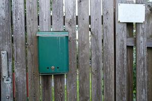 buzón, verde en una puerta de madera, un marco cuelga en la valla cercana. foto