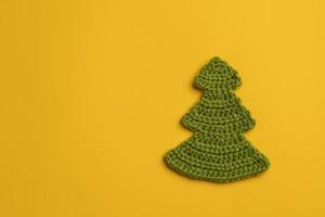 Knitted homemade Christmas tree a symbol of New Year and Xmas on a yellow background. Copy space. Holiday and magic concept. Top view. photo