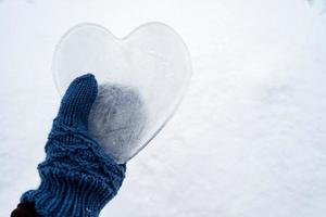 Hearts - a symbol of love, made of ice, are held by a hand in warm blue knitted mittens. Valentine's Day. Romantic concept. Copy space. photo