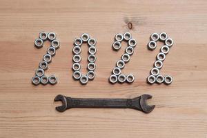 los números del año nuevo 2022 están revestidos con tuercas metálicas sobre una mesa de madera y enfatizados con una llave. vista superior. foto