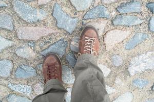 los pies en cómodos zapatos de trekking, adecuados para largas caminatas, se paran sobre adoquines antiguos. plano foto