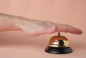 presionando el botón de llamada del servicio del hotel con la mano sobre fondo beige pastel. hotel conceptual, viajes y recreación.