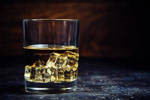 whisky enfriado de vidrio con cubitos de hielo sobre fondo de madera en bodega.