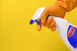 rociador para limpiar ventanas y plomería en la mano con guante sobre fondo amarillo. foto
