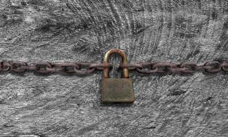 An old rusty padlock closed on a massive chain on vintage wooden table photo
