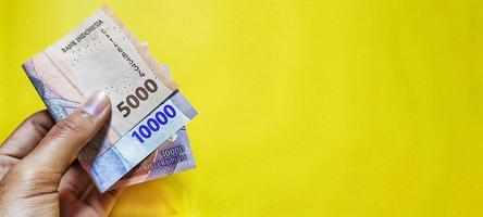 Man holding Indonesian rupiah banknotes denomination 5000 and 10000 latest edition. photo