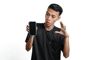 excited asian man wearing black workout t-shirt, pointing at green screen of smartphone. Isolated by white background photo