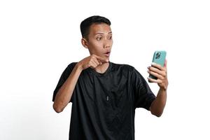 Asian man wearing black training t-shirt, With a happy excited gesture while looking at the smartphone screen. Isolated by white background photo
