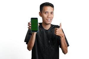 hombre asiático con camiseta negra de entrenamiento, con un gesto feliz y emocionado mientras mira la pantalla del smartphone. aislado por fondo blanco foto