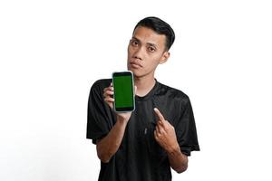 excited asian man wearing black workout t-shirt, pointing at green screen of smartphone. Isolated by white background