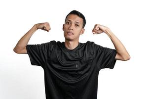 asian man wearing black training t-shirt, showing a strong stance with raised arms and muscles. Isolated by white background photo