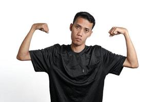 asian man wearing black training t-shirt, showing a strong stance with raised arms and muscles. Isolated by white background photo