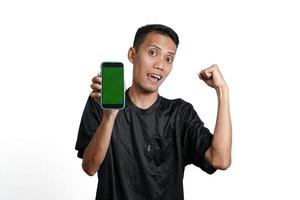 hombre asiático con camiseta negra de entrenamiento, con un gesto feliz y emocionado mientras mira la pantalla del smartphone. aislado por fondo blanco foto