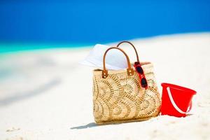 Beach accessories - straw bag, white hat and red sunglasses on the beach photo