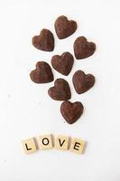 caramelos de trufa de chocolate en forma de corazón sobre un fondo blanco. amor de inscripción hecho de letras de madera. foto