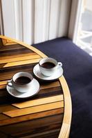 Two modern cups of espresso on a wooden table, a table in front of the window. Coffee break. photo