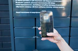 A woman picks up a parcel from a post office by scanning a QR code, online ordering, online shopping. Mail without an employee. Online sales concept. photo