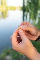 el concepto de cebo para peces. primer plano de la mano masculina de un pescador tendiendo cebo en una caña de pescar contra un lago azul. foto