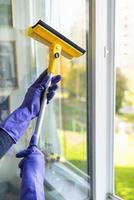 concepto de limpieza y limpieza de la casa. una joven con guantes morados y un trapeador amarillo en las manos lava la ventana.