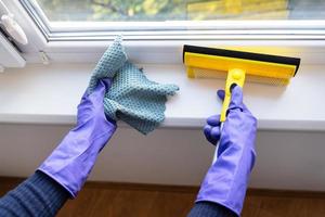 concepto de limpieza y limpieza. una joven con guantes morados sostiene un trapo y un trapeador para limpiar ventanas. foto