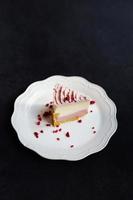 A slice of delicious raspberry cheesecake decorated with freeze-dried raspberries on a white plate stands on a dark background, top view. photo