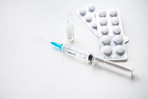 Preparation for vaccination against covid-19. Syringe, vaccine, pills, medical mask on a white table. photo