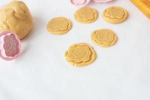 el proceso de hacer galletas con formas en forma de flores, un rodillo y una bandeja para hornear: galletas preparadas con una huella de la forma. el concepto de hornear en casa. foto