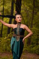 hermosa mujer asiática sosteniendo su cabello negro mientras está de pie frente al bosque con un traje verde foto