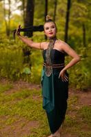 Beautiful Asian woman holding her black hair while standing in front of the forest in a green costume photo