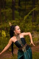 Indonesian woman with long black hair wearing a green costume with makeup in front of the forest photo