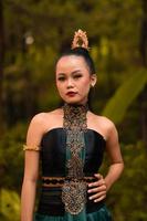 Indonesian woman with the green dress and make-up on her face standing in front of the jungle photo