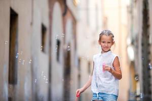 Little girl blowing soap bubbles in european city. Portrait of caucasian kid enjoy summer vacation in Italy photo